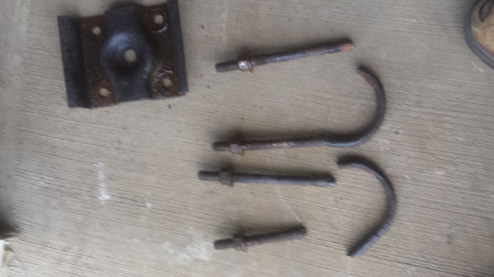 Spring shackle bracket, U-bolts, and threaded bolts laid on a wood surface