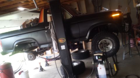 Black truck raised on a two-post lift in a garage with spare tires