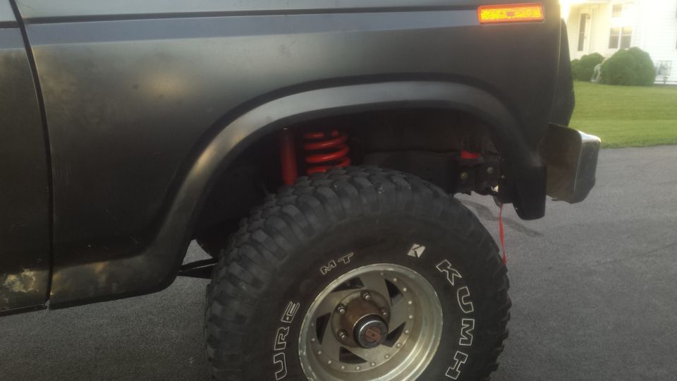 Rear quarter photo of a lifted Bronco showing red coil spring and tire