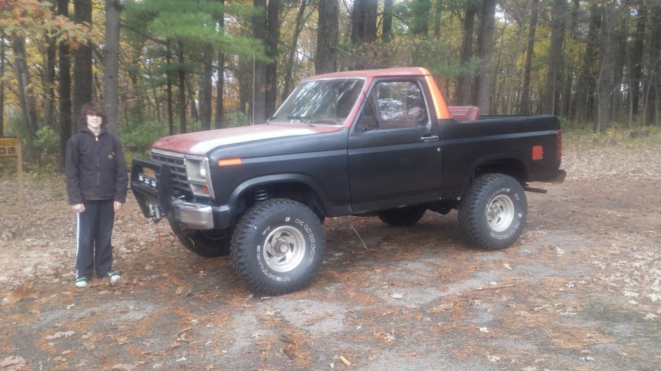 Photo of a person standing beside a black lifted Bronco in the woods