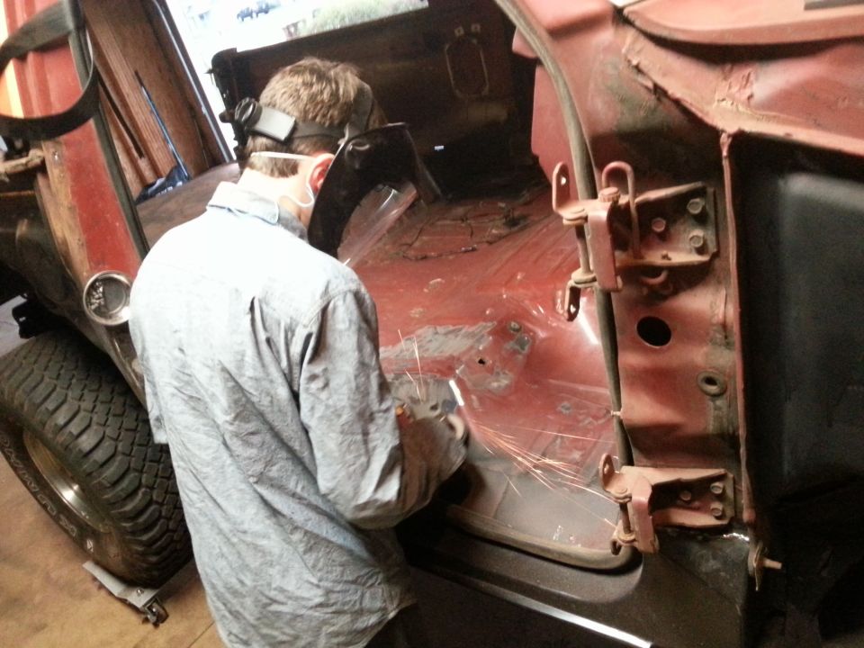 Photo of a person grinding metal on a red truck body in a shop