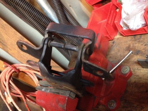 Photo of a black metal mount or hinge bracket clamped in a red bench vise