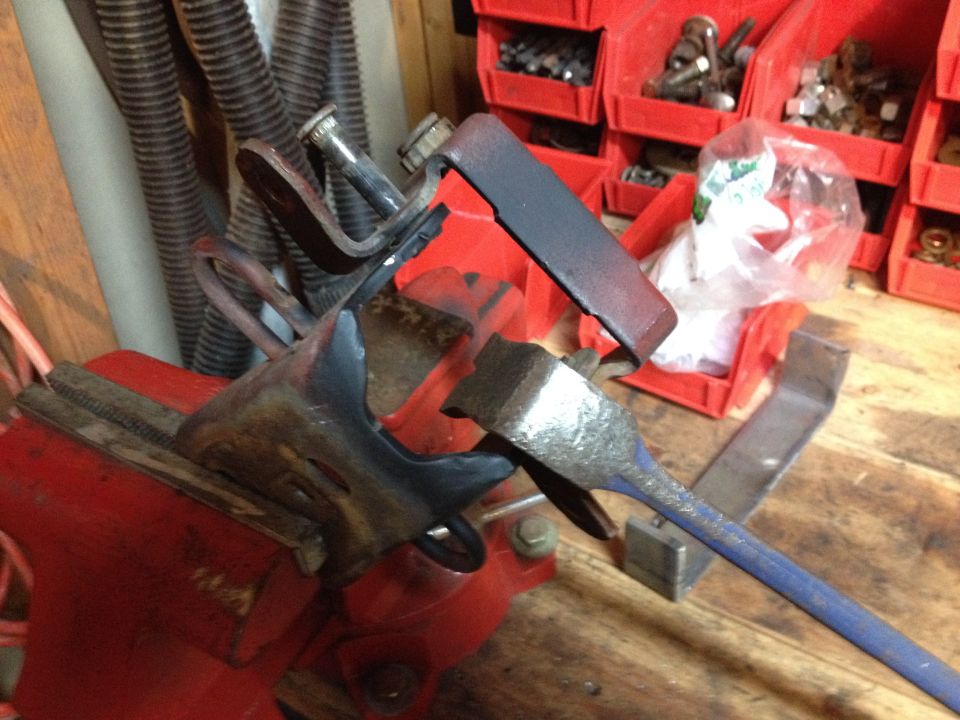 Photo of a metal bracket clamped in a vise being worked with a tool