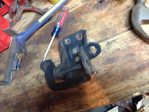 Photo of a black door hinge bracket with a screwdriver on a workbench
