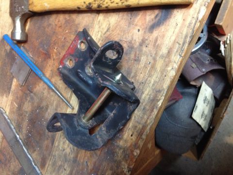 Photo of a black hinge bracket and pin on a workbench with hammer and punch