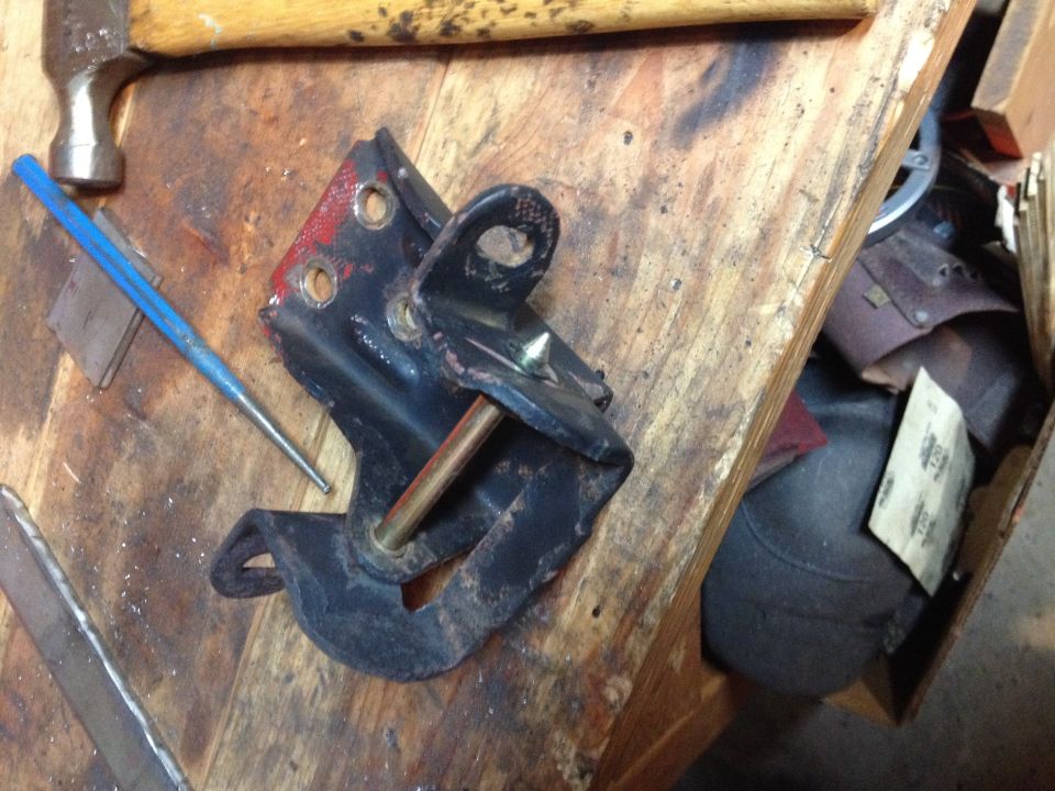 Photo of a black hinge bracket and pin on a workbench with hammer and punch