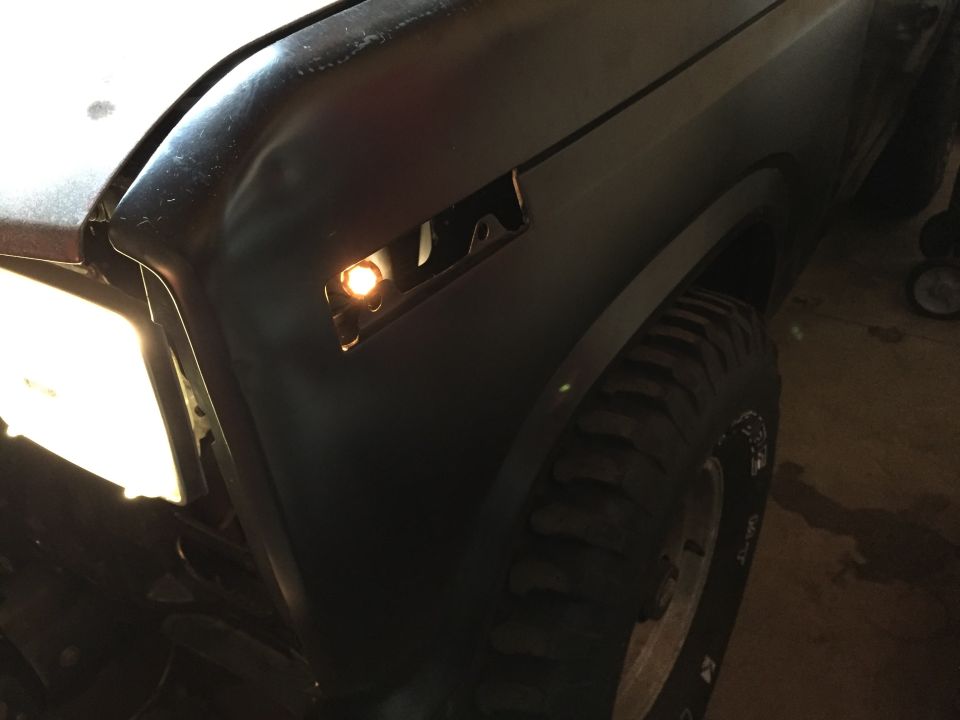 Black truck front fender with marker light illuminated, in a garage