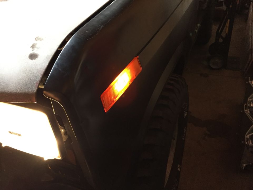 Truck fender with amber side marker light lit, in a dim garage