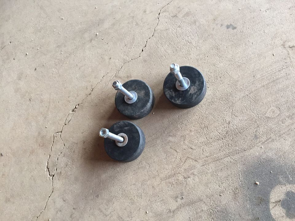 Three rubber bump-stop mounts with studs lying on a concrete floor