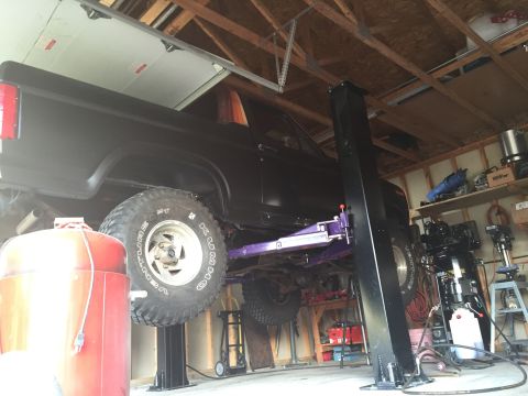 Black truck raised on a two-post lift inside a garage