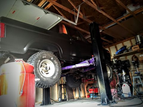 Black truck raised on a two-post lift inside a workshop garage
