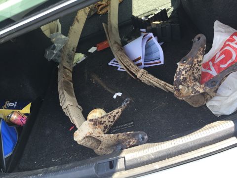 Rusty leaf springs and brackets lying in a carpeted car trunk