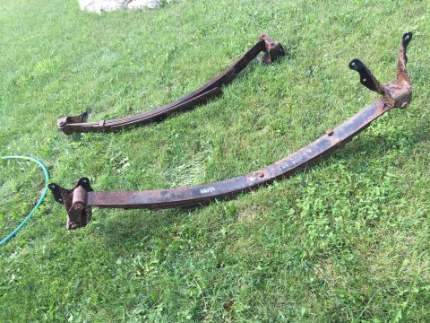 Two rusty leaf-spring assemblies lying on grass