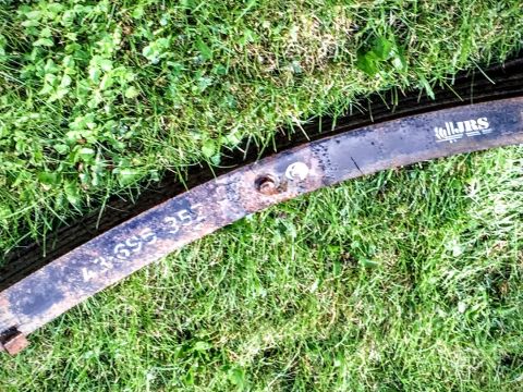 Close-up of a rusty leaf spring with painted markings, lying on grass