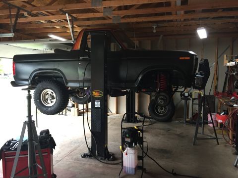 Dark-colored Ford Bronco on a lift, viewed from the side