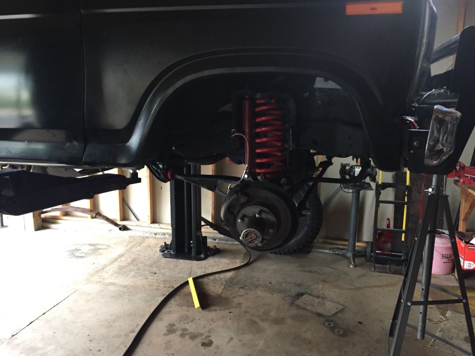 Black SUV chassis on lift, showing suspension and red coil spring