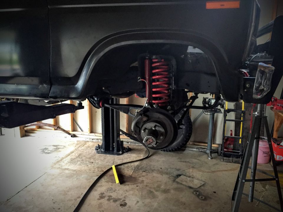 Front suspension and brake assembly of a vehicle on a lift, showing red coil springs and brake rotors