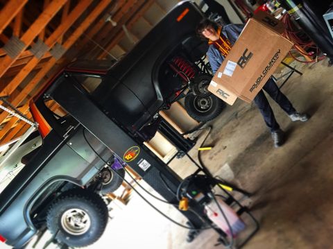 Person carrying a Rough Country box beside a truck in a garage