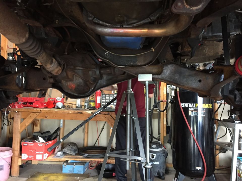 Underside of a vehicle with a differential, exhaust, and suspension parts supported by a jack