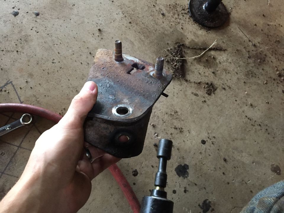 Hand holding a rusty bracket or mount over a garage floor