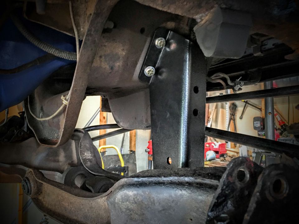 Black bracket bolted to a vehicle frame, underside view