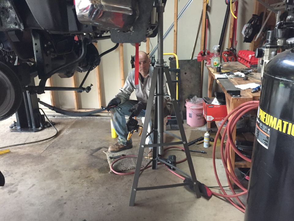 Person kneeling under a lifted truck in a garage during suspension work