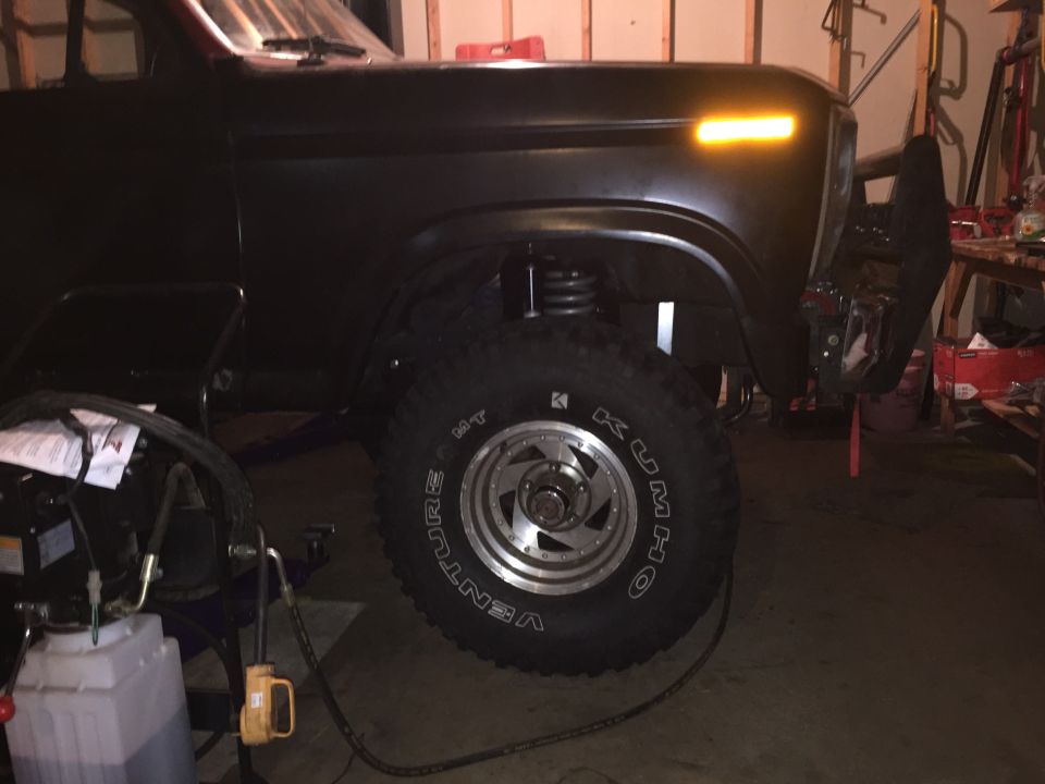 Front fender and wheel of a black lifted Ford Bronco in a garage