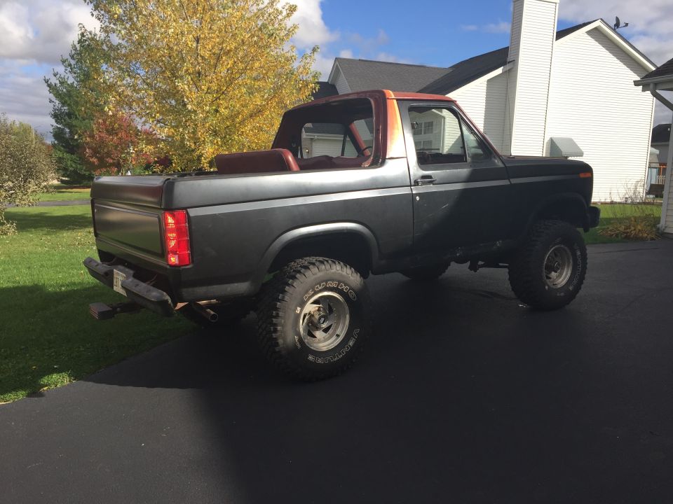 Rear three-quarter view of a primer-black lifted Ford Bronco in a driveway