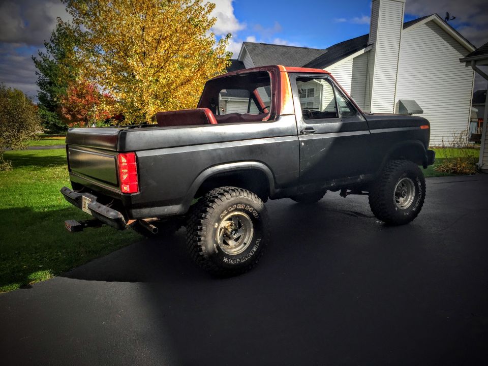 Rear three-quarter view of a lifted Ford Bronco in a driveway in autumn