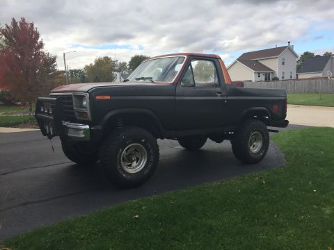 Front three-quarter view of a lifted Ford Bronco in a driveway under cloudy sky