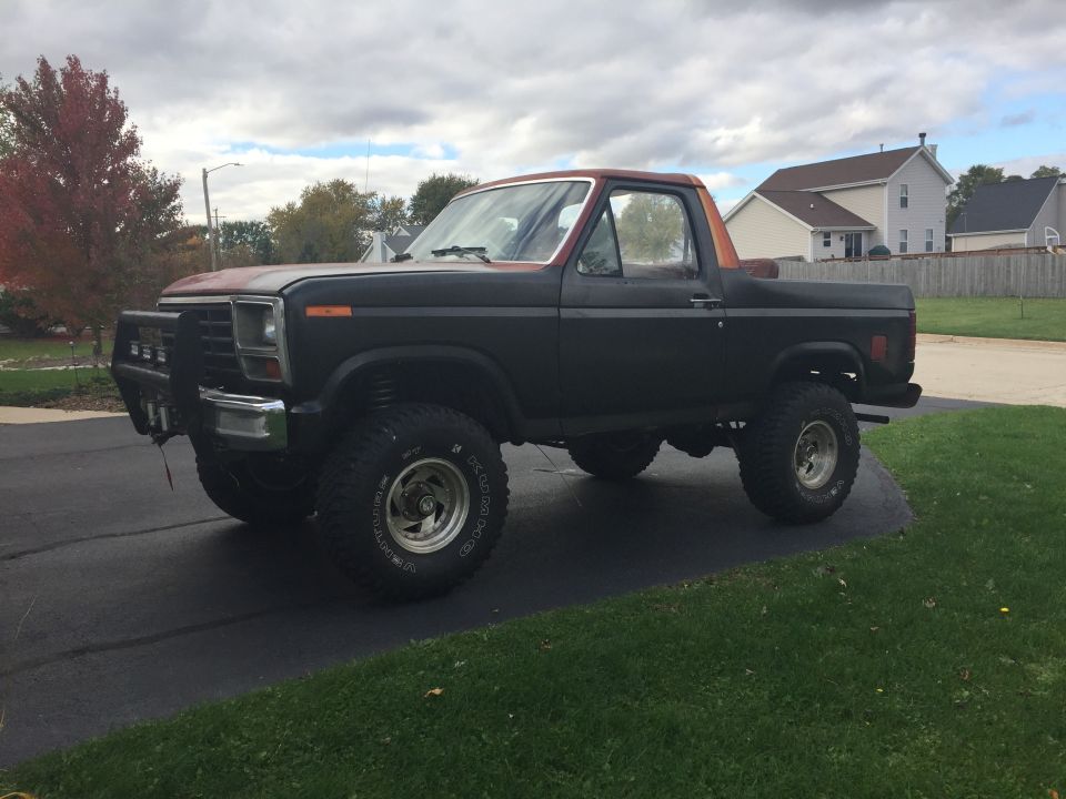 Front three-quarter view of a lifted Ford Bronco in a driveway under cloudy sky