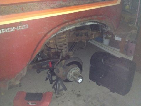 Front wheel well of a red Bronco with exposed spindle and coil spring