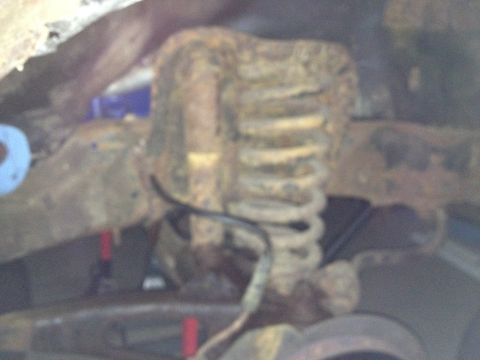 Close-up of a heavily rusted coil spring and frame under a vehicle