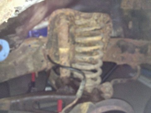Close-up of a rusted coil spring and bracket on a vehicle underbody