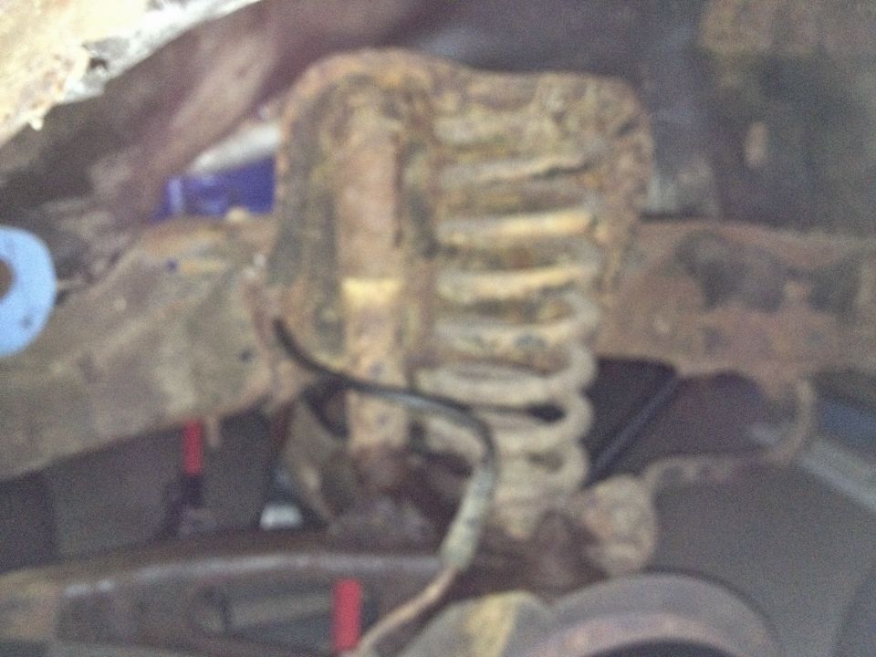 Close-up of a rusted coil spring and bracket on a vehicle underbody