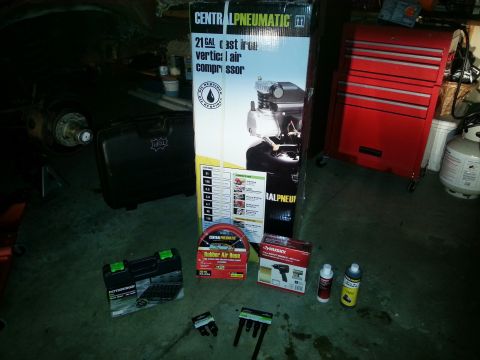 Central Pneumatic air compressor box and tools staged on a garage floor