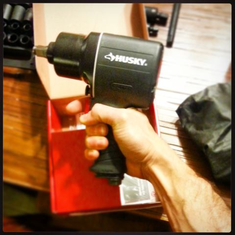 Hand holding a black Husky air impact wrench over its red box