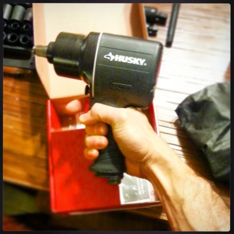 Hand holding a Husky air impact wrench with sockets in background