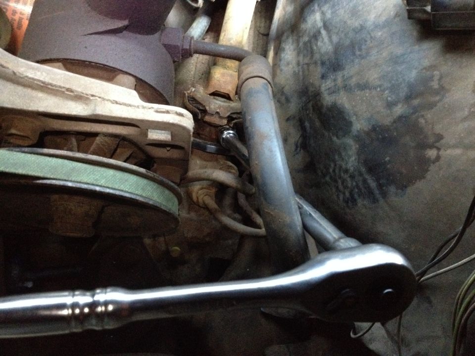 Ratchet wrench working on engine components, near a belt and pulley