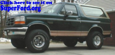 1995 Ford Bronco - A dark green Ford Bronco with tan side trim is parked in front of a garage.