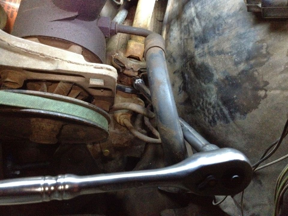 Engine bay with a socket wrench on a bolt, green belt, and rusty metal