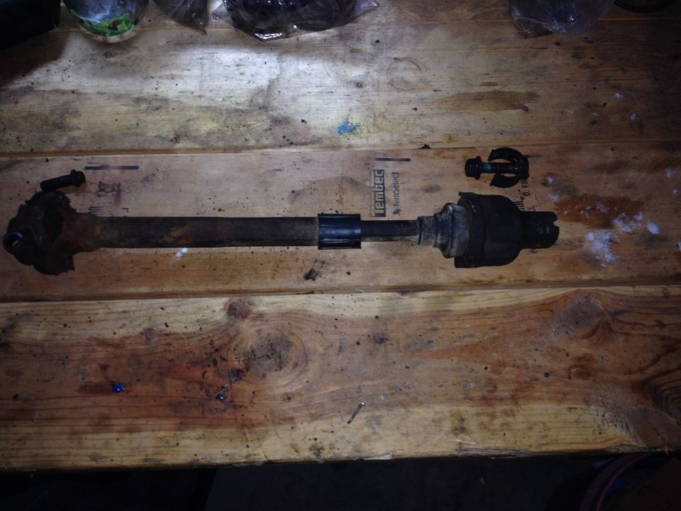 Drive shaft part on a wooden surface with "SUPERMOTORS.NET" visible