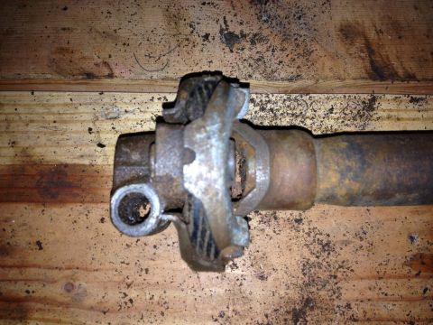 Close-up of a rusty driveshaft U-joint on a wooden surface. Supermotors.net logo visible