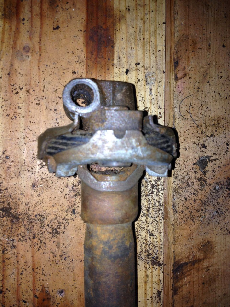 Driveshaft universal joint with rust and wear, mounted on a wooden background