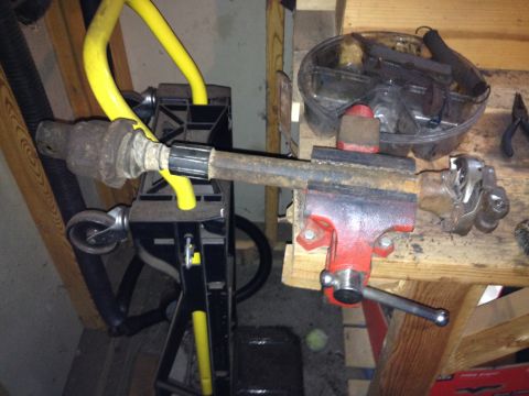 Driveshaft part clamped in a red vise, with yellow hose and black stand