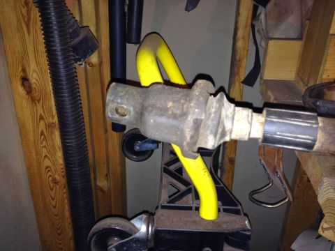 Close-up of a rusty metal vehicle axle part with a yellow protective cover, resting on a black stand with whee