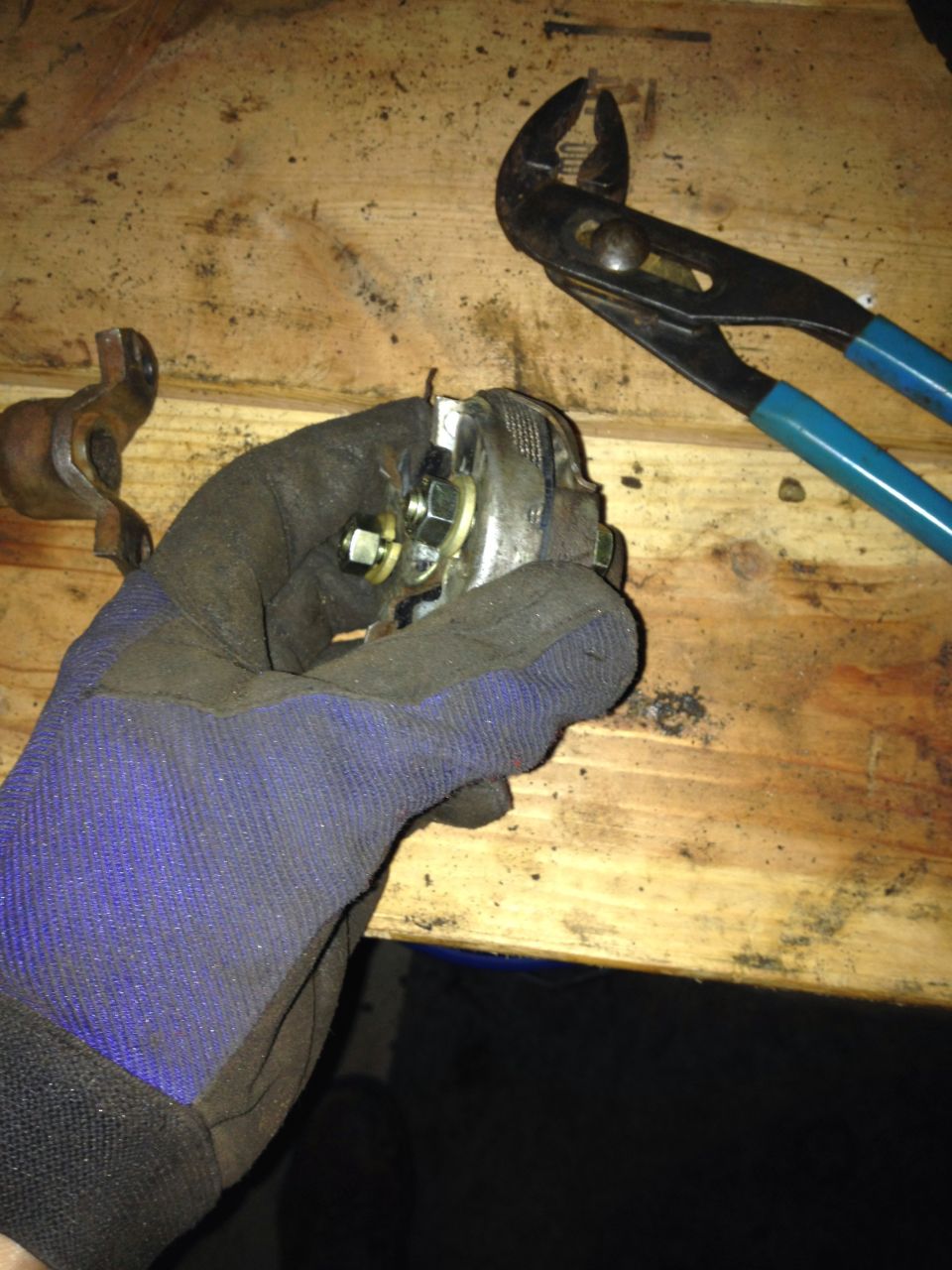 Gloved hand holding a small valve part next to pliers on a workbench