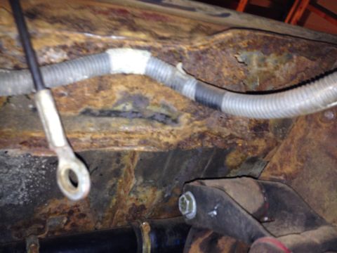 Photo of a rusty floor pan with corrugated hose and mounting bracket