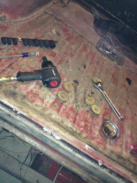 Photo of an impact wrench, wrench, and sockets on a vehicle floor pan