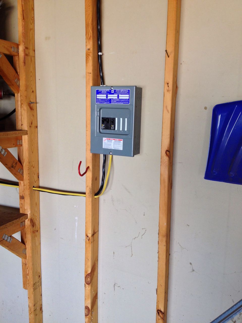 Photo of a small electrical breaker panel mounted on a garage wall stud